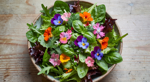 Overhead view of a colorful salad bowl with fresh greens, herbs, and edible flowers